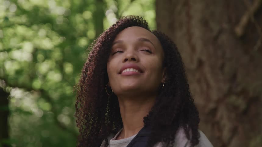 A hiker smiles as she looks up and takes in the forest around her