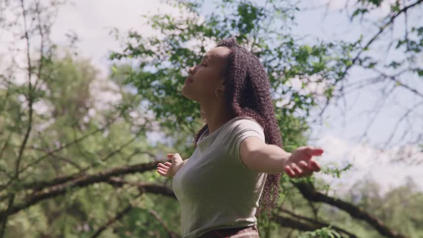 A woman standing near trees with her arms outstretched