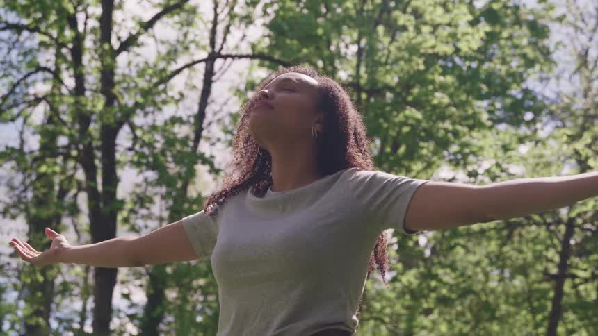 A young black woman faces the sky with her eyes closed and her arms held wide