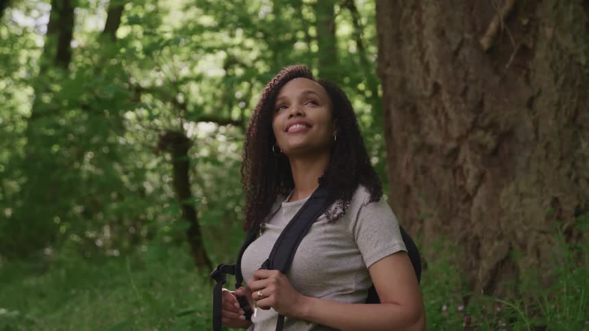 A young woman in a forest looks up and smiles