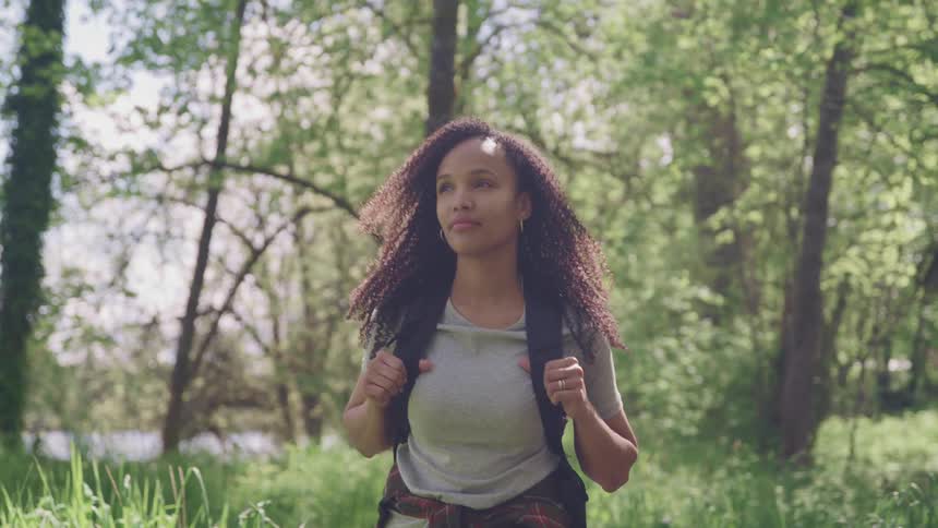 A woman looks around and smiles as she hikes through a forest
