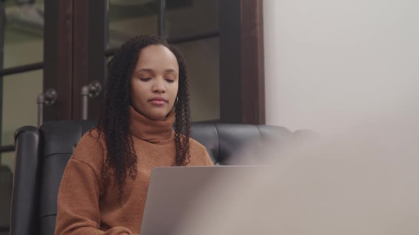 A woman sitting on a couch in front of a laptop with a door behind her