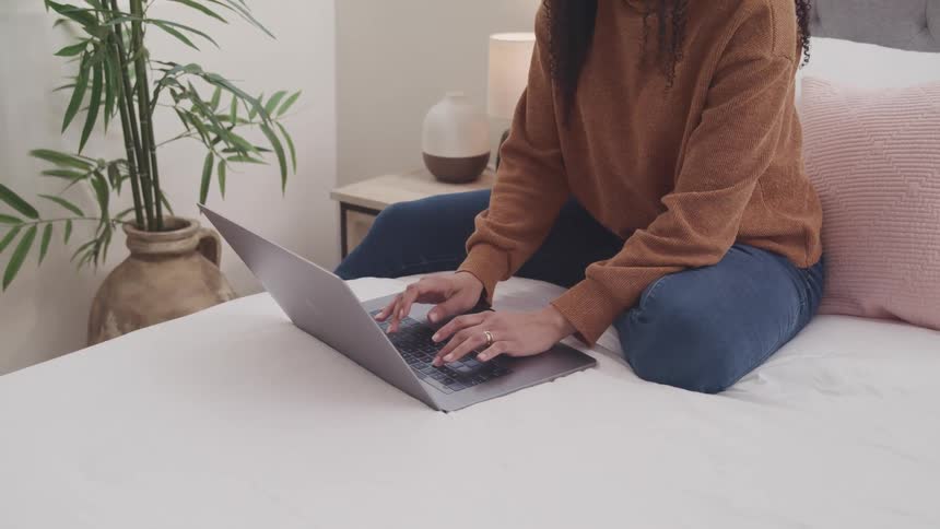 A woman is typing on her laptop in bed
