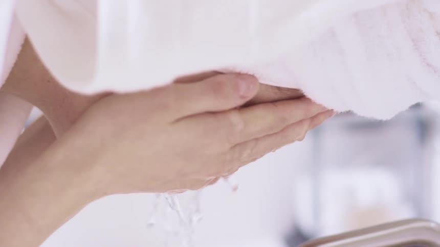 Woman wearing a white bathrobe washes her face with water in the bathroom