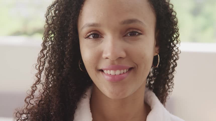Black woman with curly hair turns her head and faces the camera with eye contact