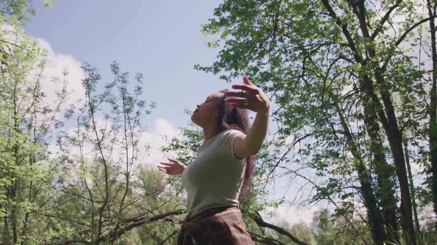 A woman stretches her arms out as she stands in a forest