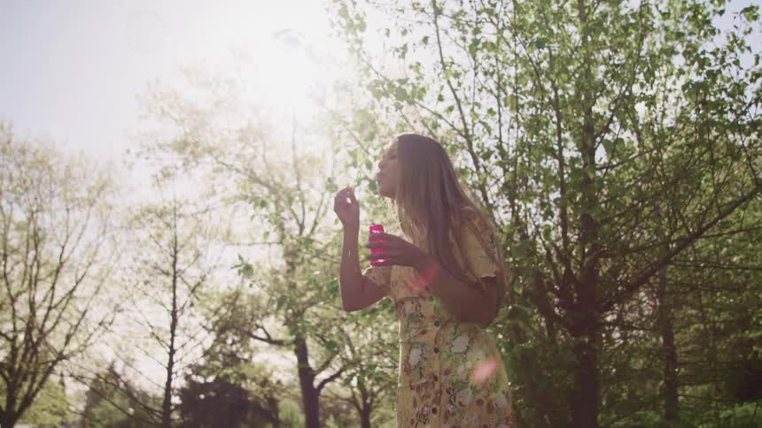 A woman uses a bubble wand to bubbles outdoors in a woodland on a sunny day
