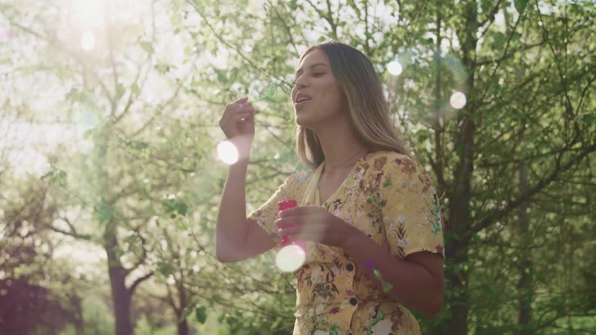 A teenage girl blows bubbles in a forest