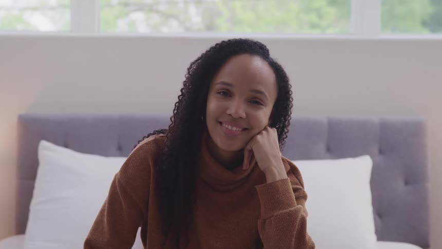 Smiling woman looks at the camera while sitting on a bed in the bedroom