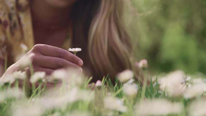 Woman holds a flower and twirls it around with her fingers