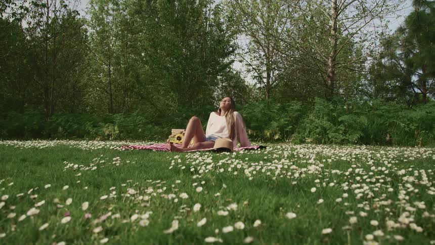 A teenage girl sits on a blanket in a field of flowers