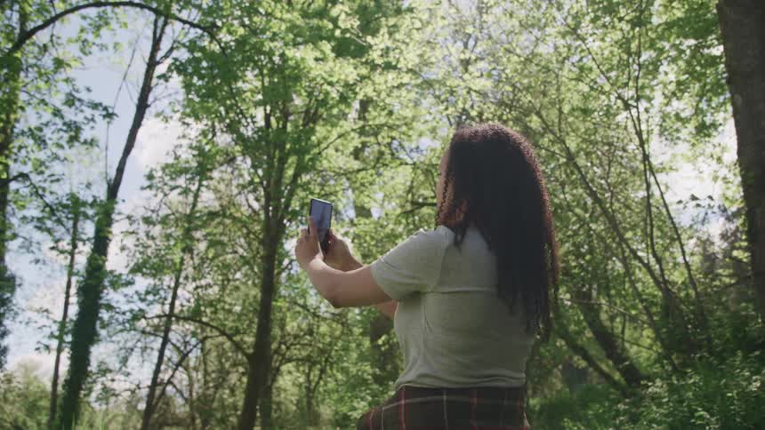 Woman takes a selfie with a smartphone while sitting in the forest