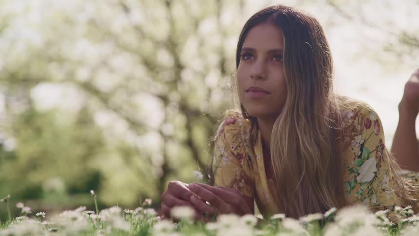Woman lies on stomach in field playing with flowers and looking up