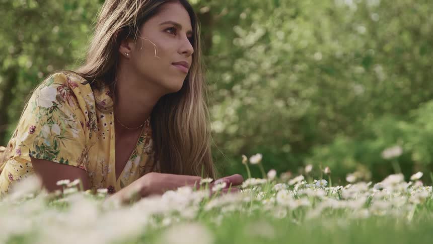 Woman lays on the ground in a prairie filled with white wild flowers