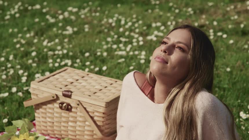 Woman leans back looking at sky basking in sun while having a picnic in a wildflower strewn meadow