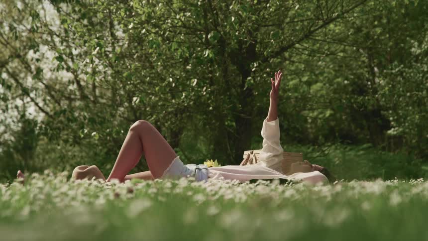 A teenager lying in a grassy field reaches her arm up towards the sky