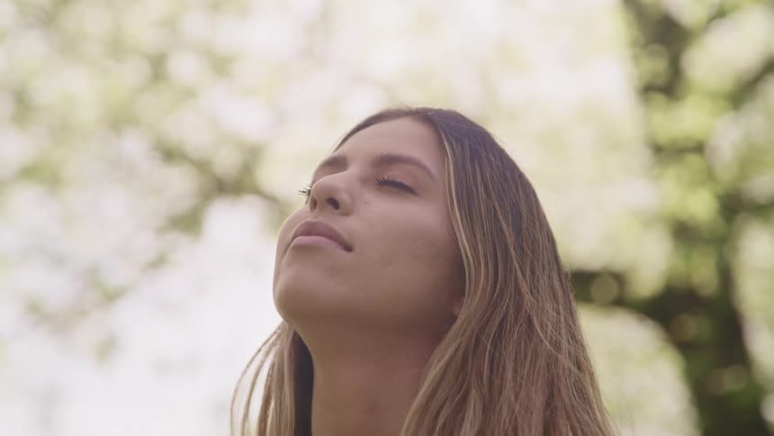 A teenage girl outside closes her eyes as she looks up