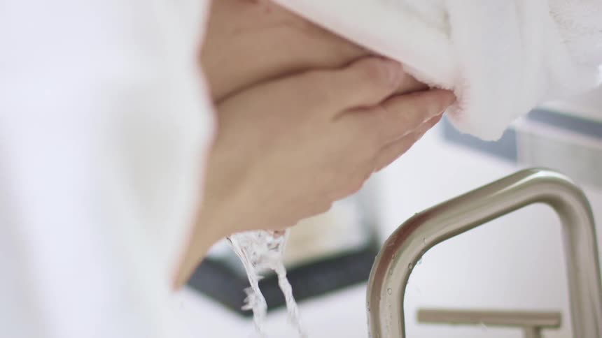 Woman wearing a bathrobe washes her face in the bathroom