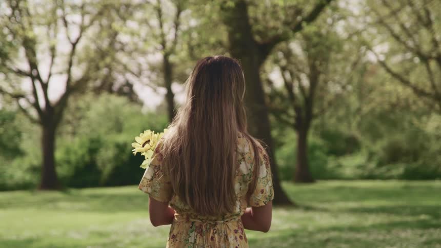 Woman stands looking at field and trees holding a bouquet