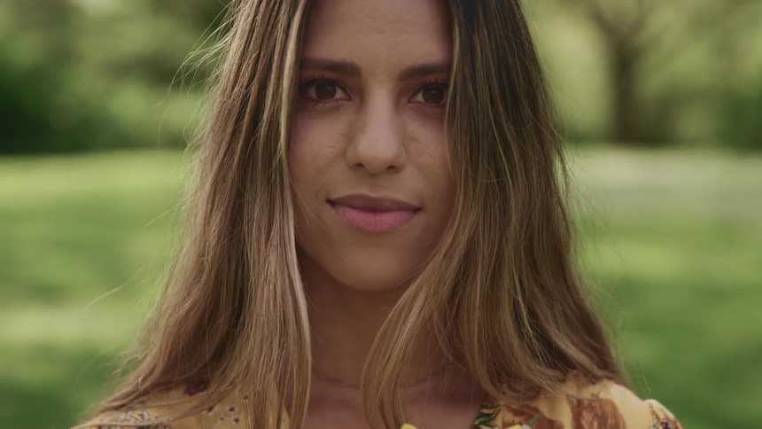A woman stands in an open field and holds a large yellow flower