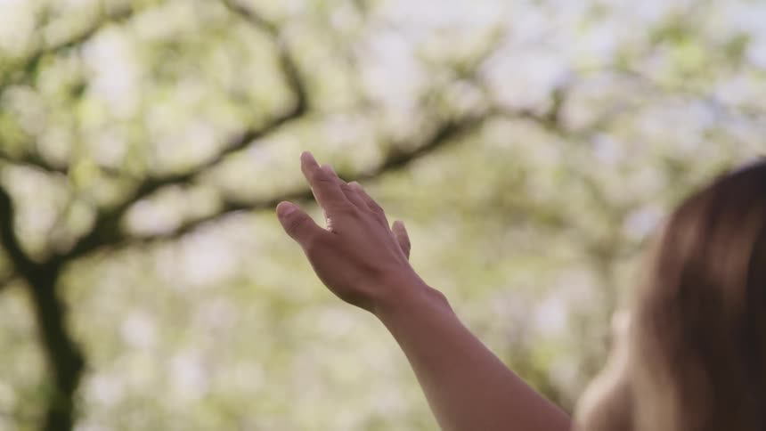 Woman extends her arm and opens her hand on the air in front of trees outdoors