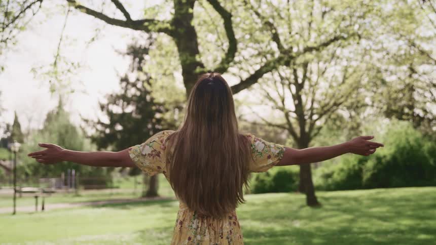 A teenage girl standing outside raises her hands to her side