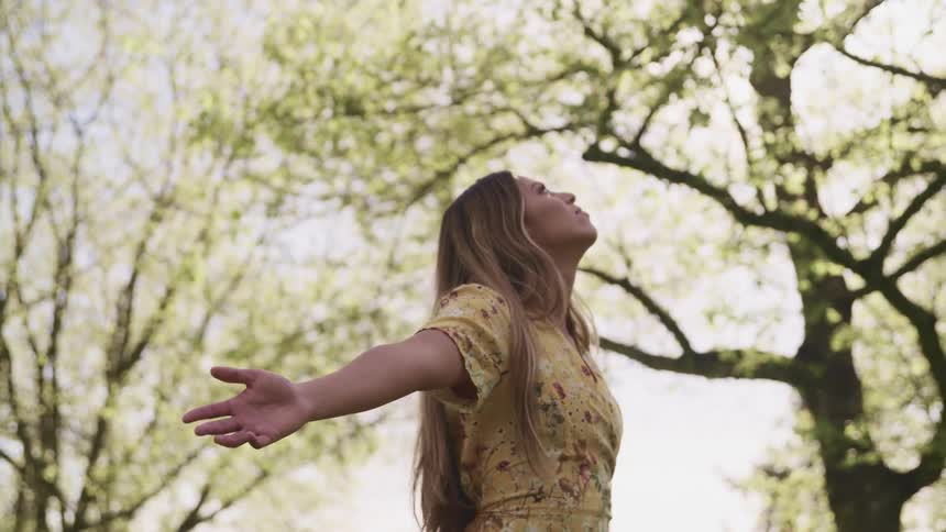 Woman stands with arms wide open looking at the sky near the trees outdoors