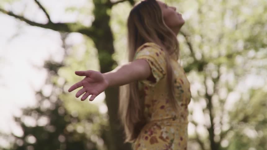 A young woman stands under the trees and stretches her arms out to her side