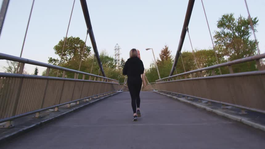 A woman in a jogging suit runs across a bridge during the day