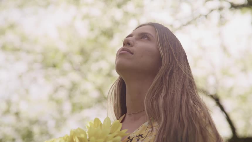 A female teenager holding flowers looks up towards the sky