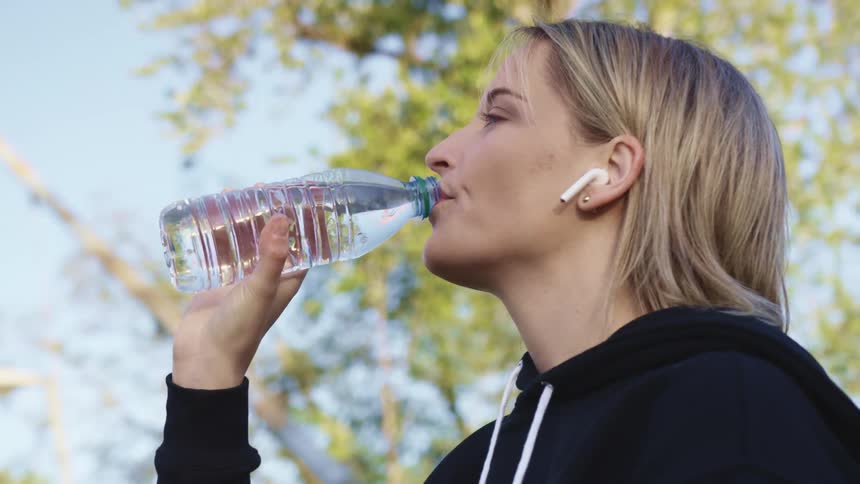 A young woman outside drinks out of a bottle of water