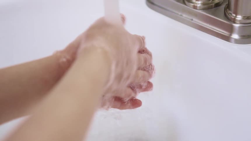 A person washing their hands under the running water of a faucet