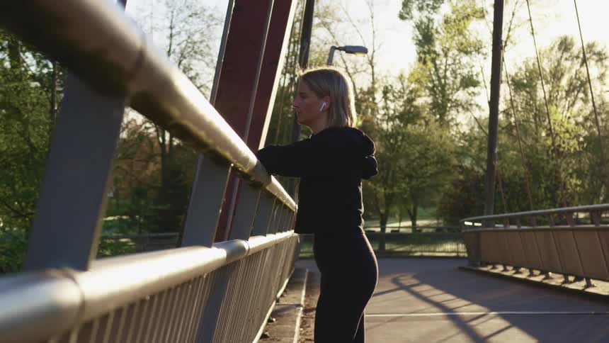 A woman standing on a bridge with ear buds in looks off in to the distance