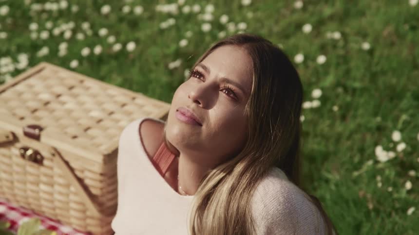 Woman looking up to the sky while sitting in the grass near a picnic basket