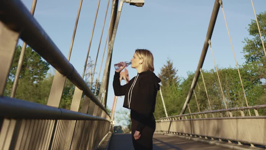 A woman drinking water on a bridge
