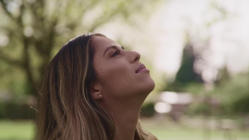 Side view of a woman with brown hair and earrings looking up at sky in a public park