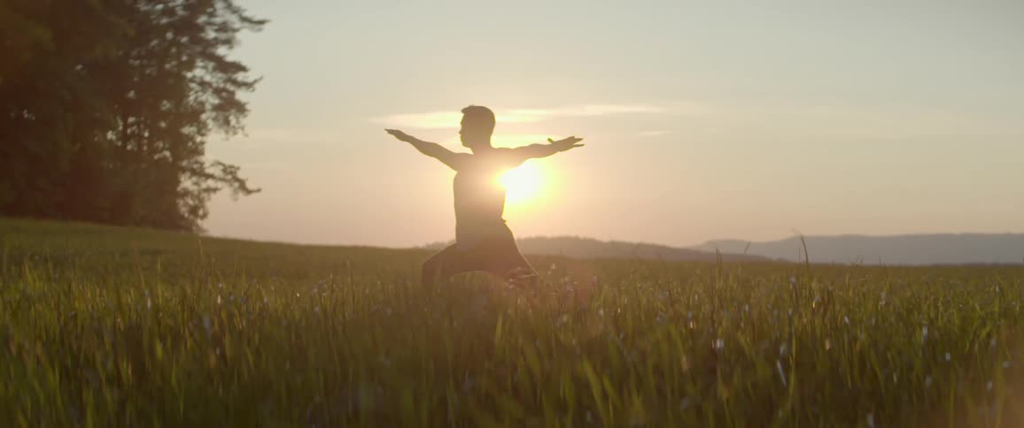 A man stands in a field raising and stretching his arms in meditation pose