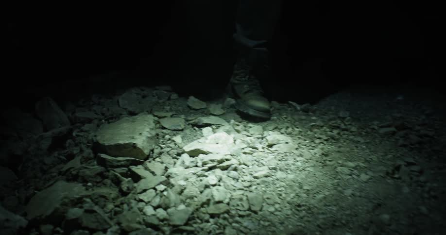 A man walks through a rocky area with a flashlight at night