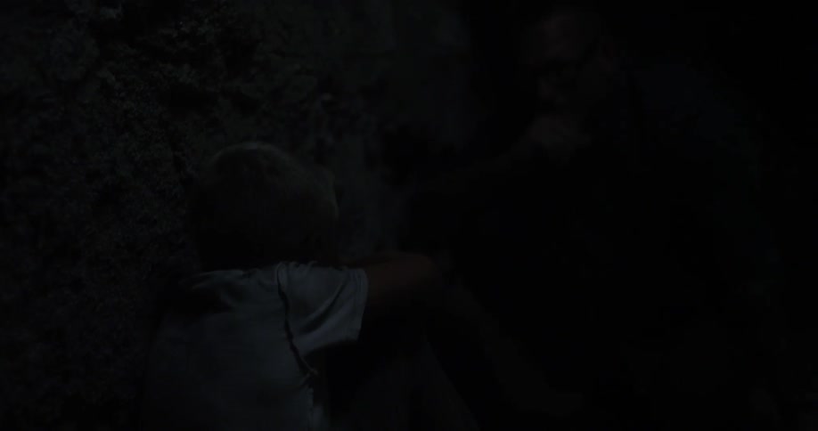 A child crouches against a wall in a dark cave