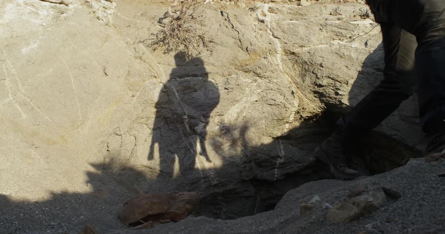 A man emerges from a ground cave with a boy on his back