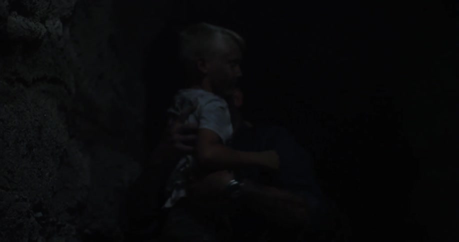 A hand helps a boy climb up in a dark area