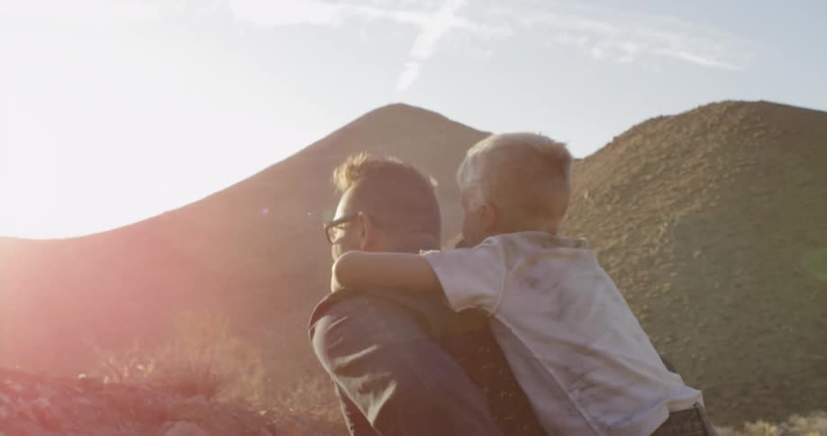 A man carries a child on his back up a mountain in the daytime