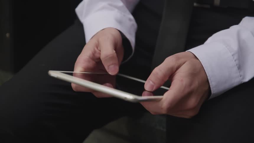 Businessman with a suit sits down and uses a tablet