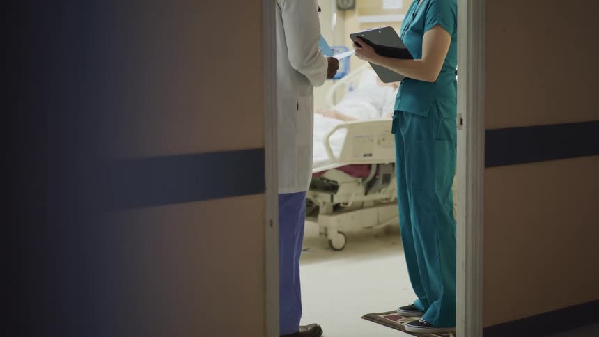Nurse and doctor talk to each other in the door of a hospital room