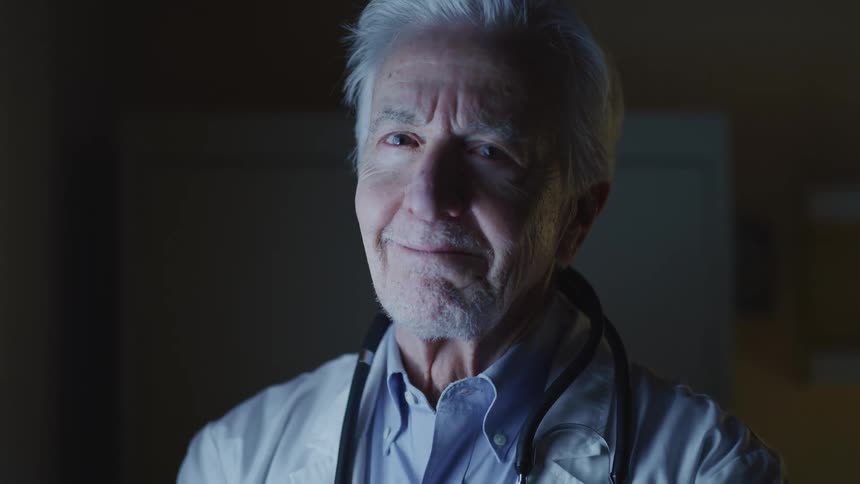 A doctor with a stethoscope around his neck turns his head and smiles