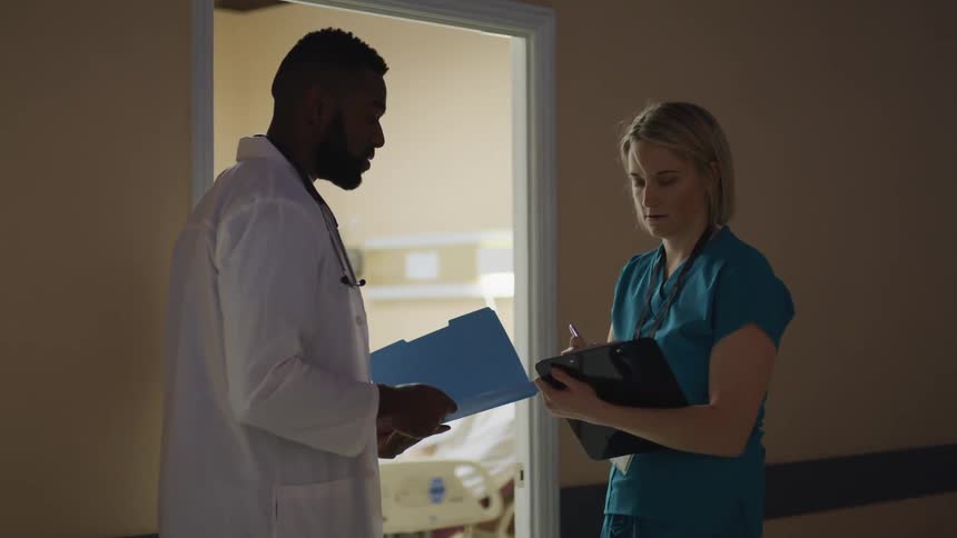A doctor and nurse talk outside a patients room