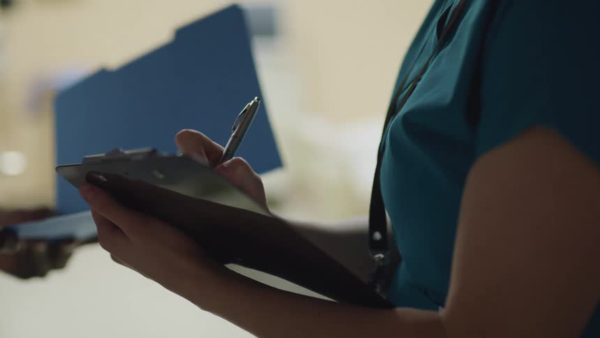 A nurse writes on a chart as she talks with a doctor