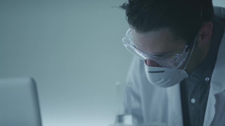 A doctor writes as he looks at a laptop
