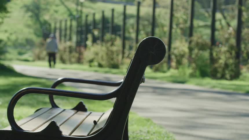 Close up of a metal bench in a public park with a man walking away in the background
