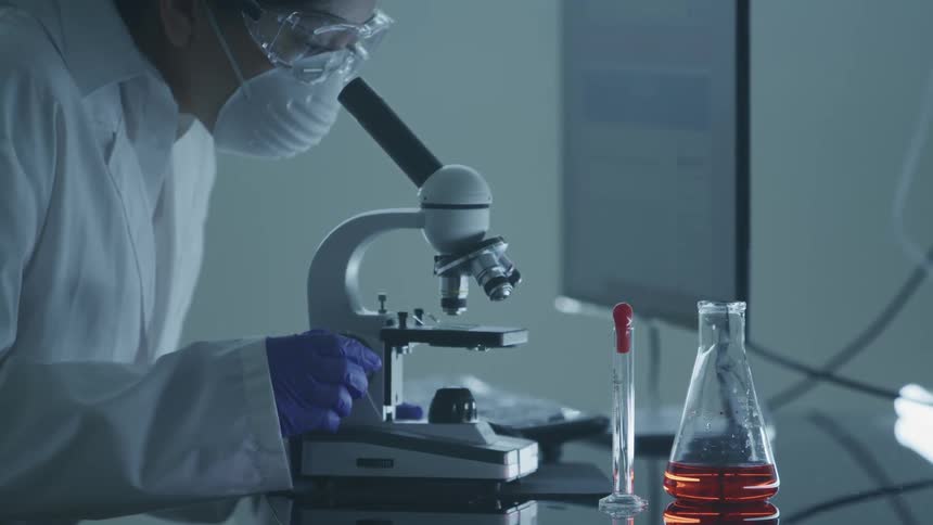 A lab technician is working on a computer and microscope